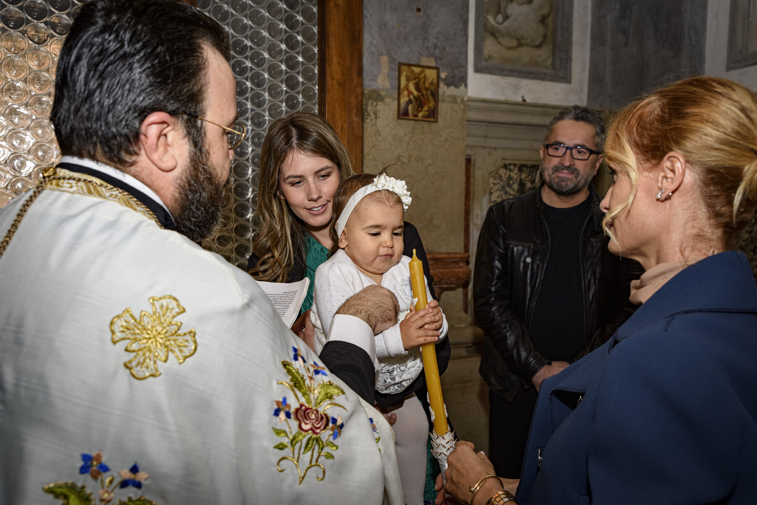 Bambina con candela battesimo ortodosso circondata dai parenti, progetto Storie da condividere a Padova
