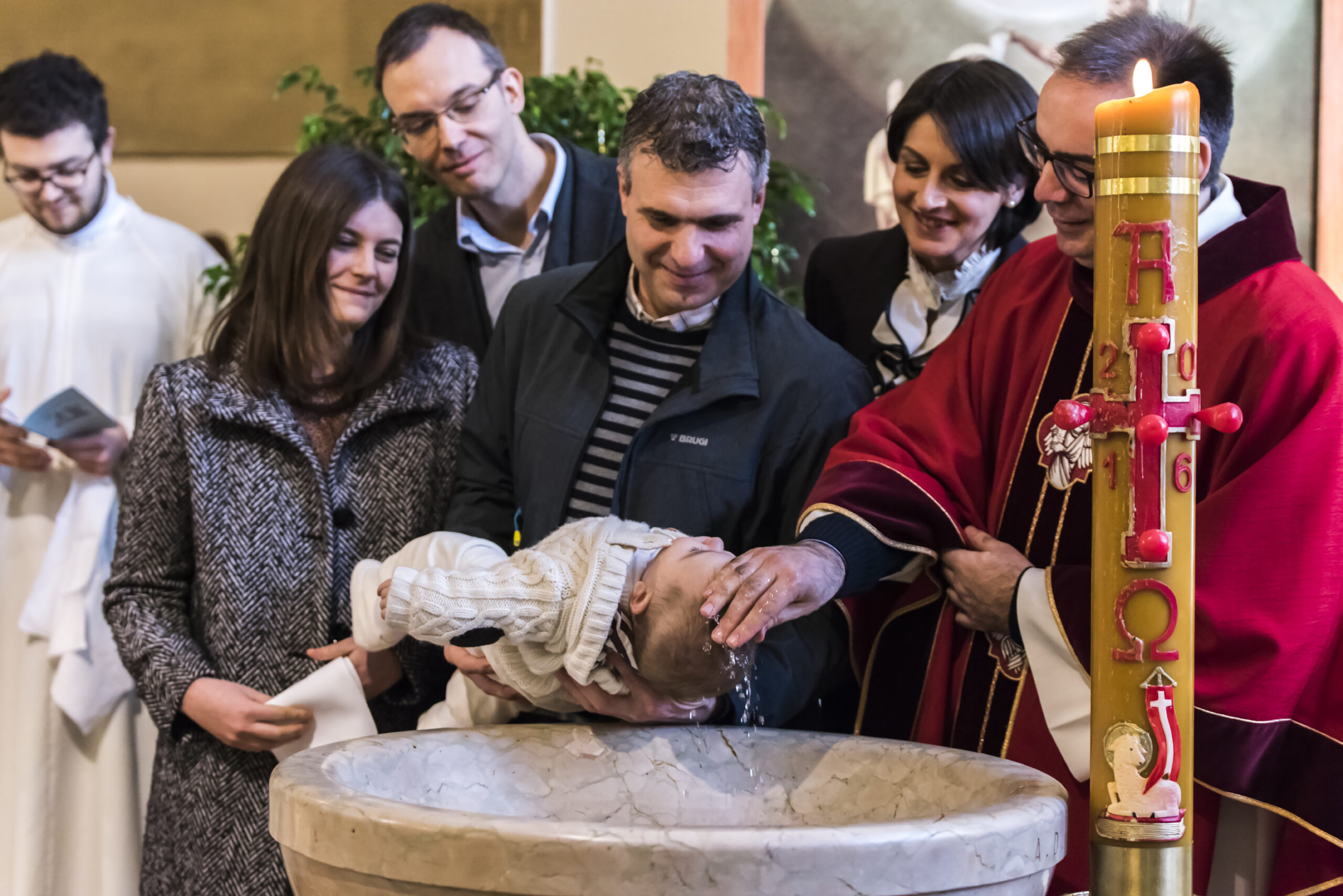 Celebrazione del battesimo con il neonato al fonte battesimale, progetto Storie da condividere a Padova
