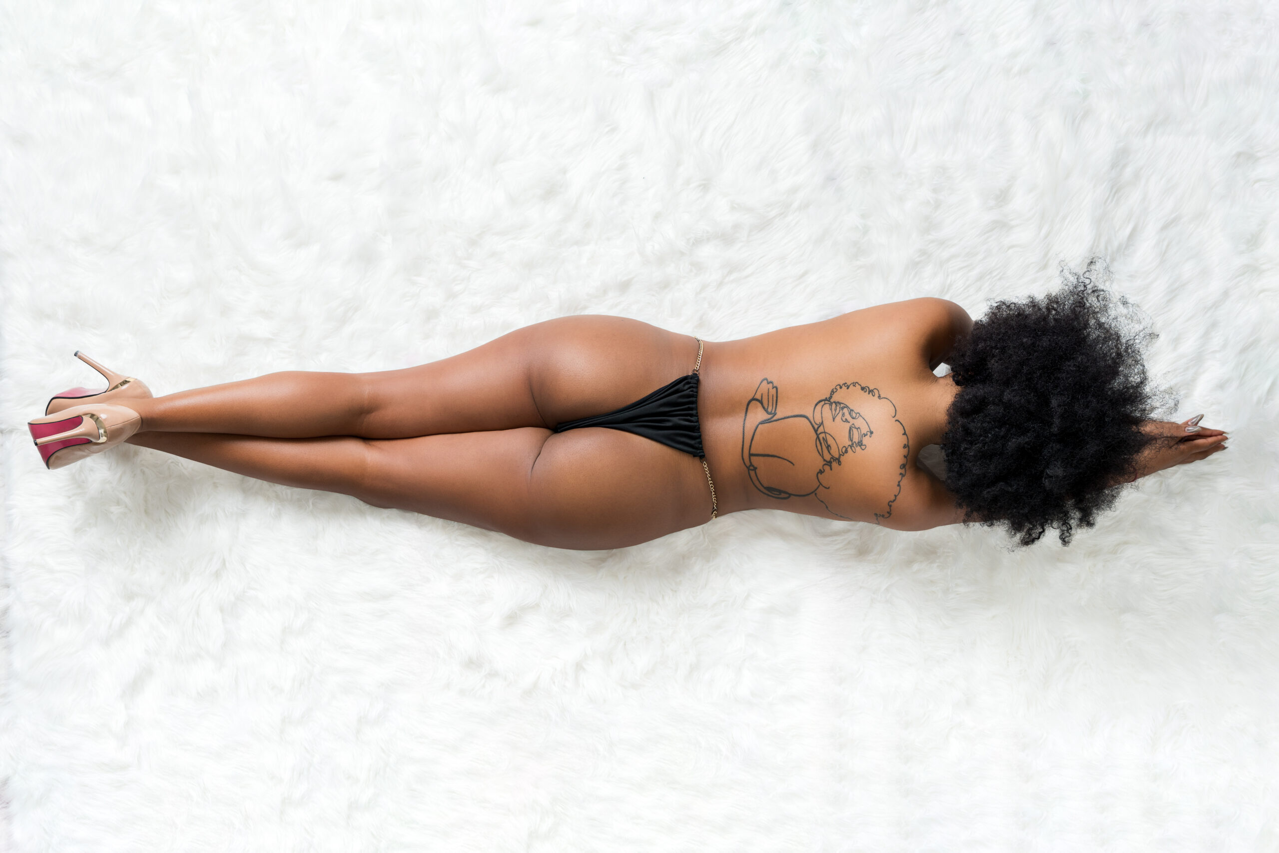 Ritratto dall’alto di schiena su tappeto bianco con tatuaggio e scarpe con tacco, servizio boudoir a Padova