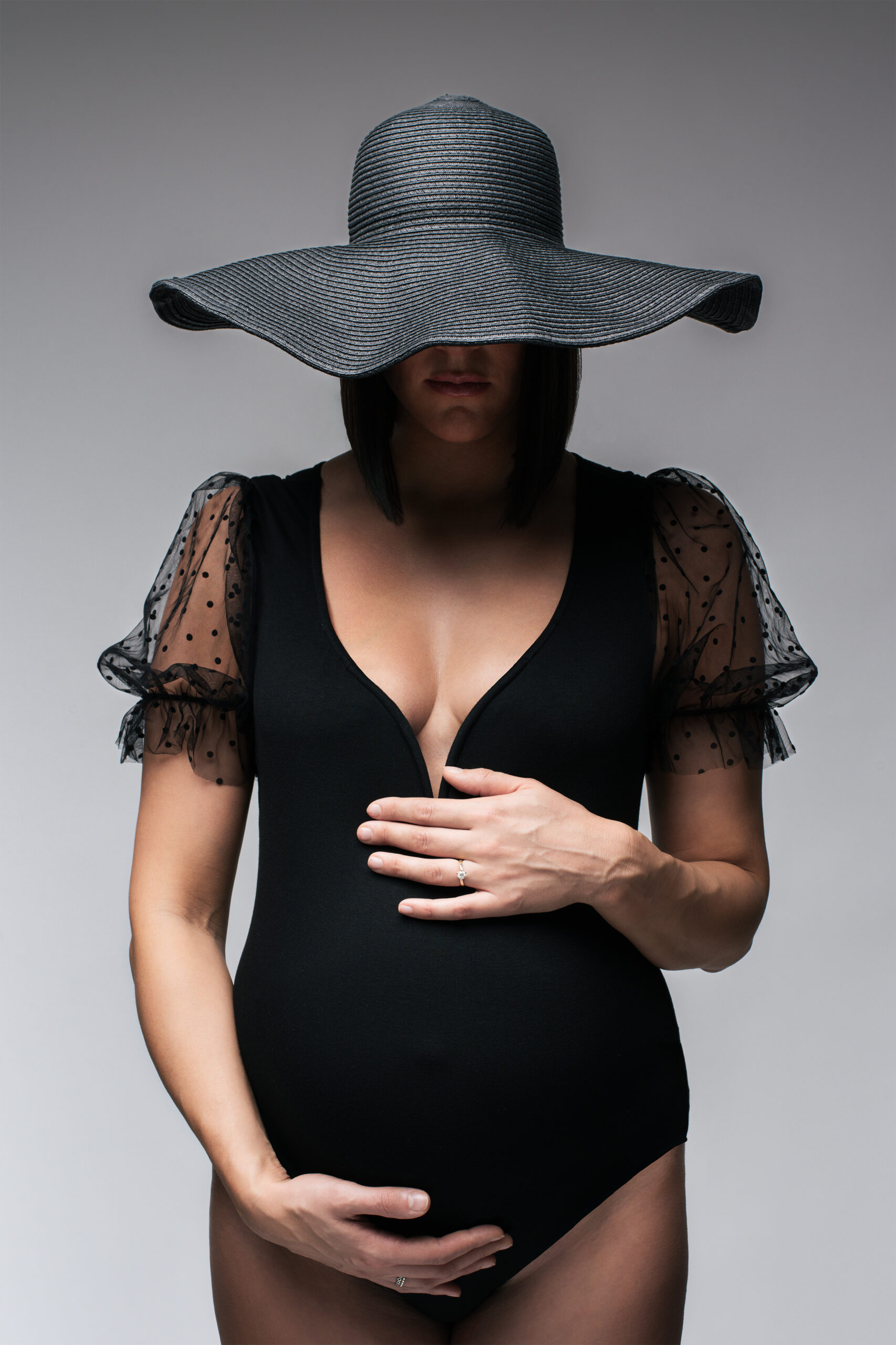Ritratto creativo di futura mamma con cappello nero e mani sul pancione, progetto Storie che iniziano a Padova
