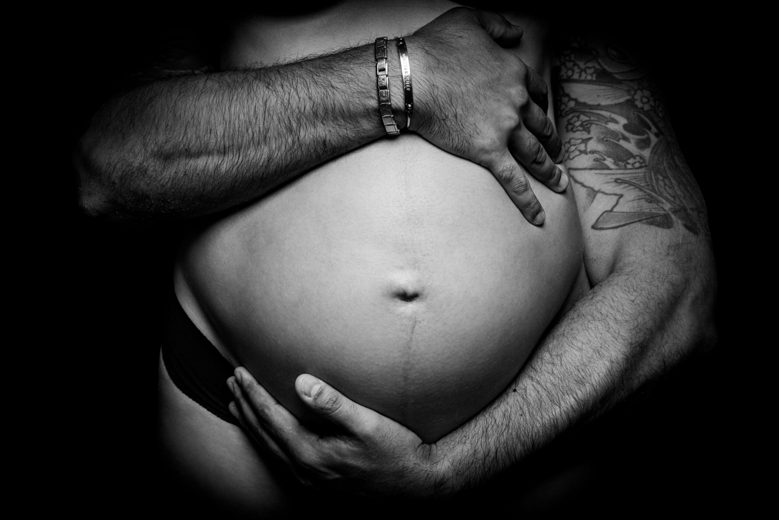 Primo piano in bianco e nero del futuro papà che abbraccia il pancione, progetto Storie che iniziano a Padova