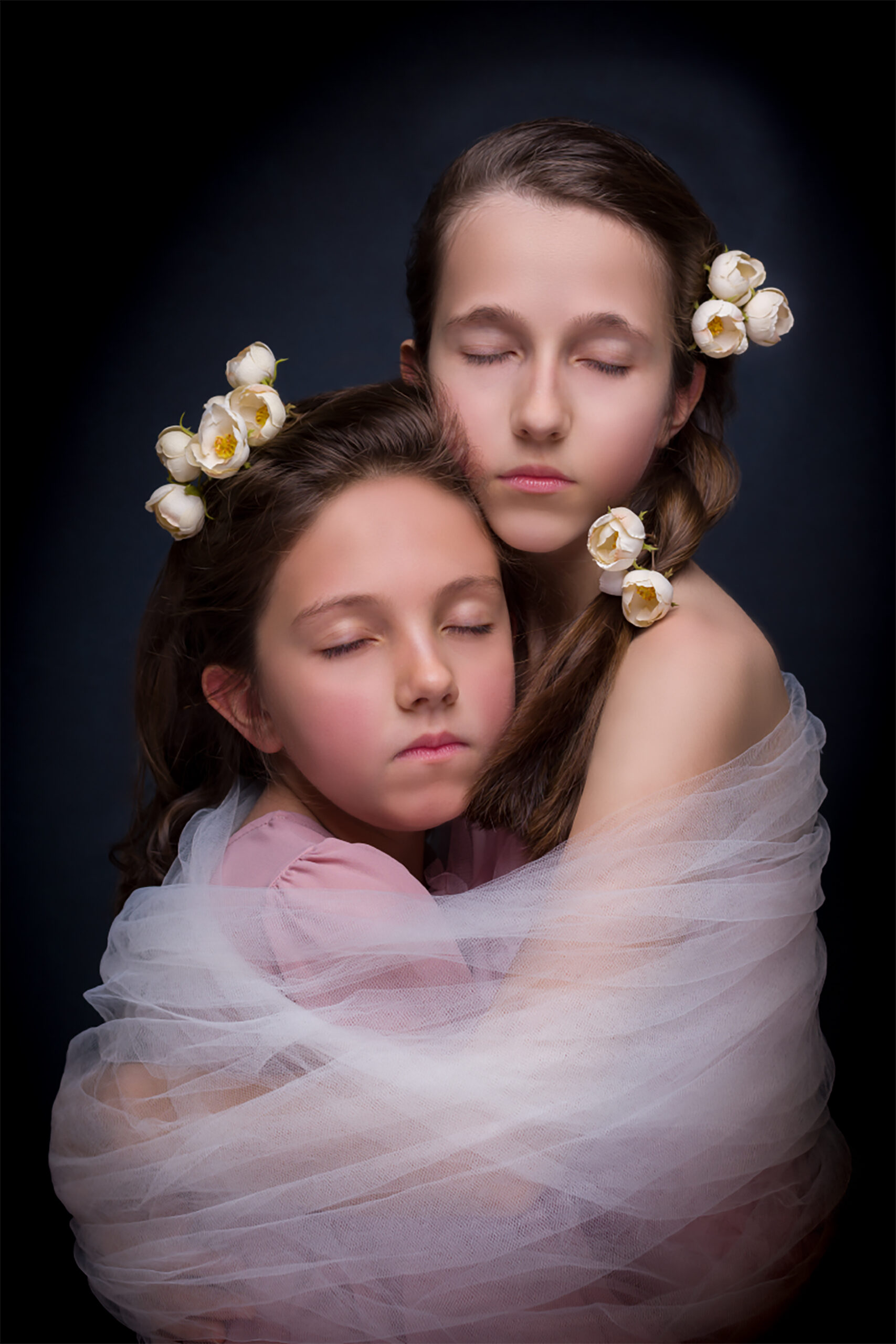 Ritratto fine art di due bambine con fiori bianchi e tulle rosa su sfondo scuro a Padova