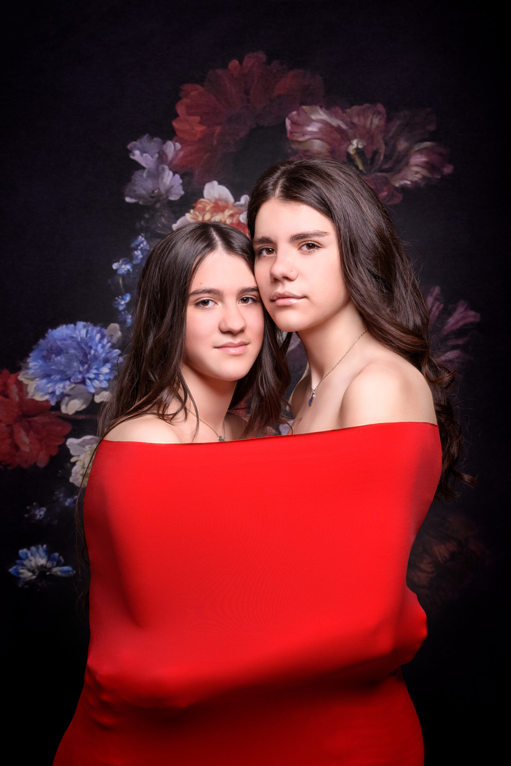 Ritratto fine art di due sorelle davanti a uno sfondo floreale, avvolte in un drappo rosso a Padova